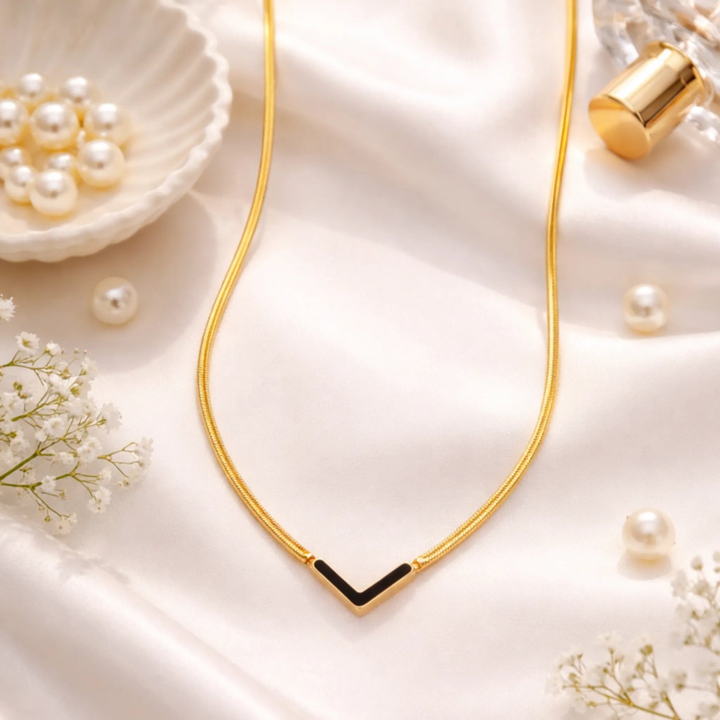 Gold necklace with a black accent on a soft white background with pearls and flowers.