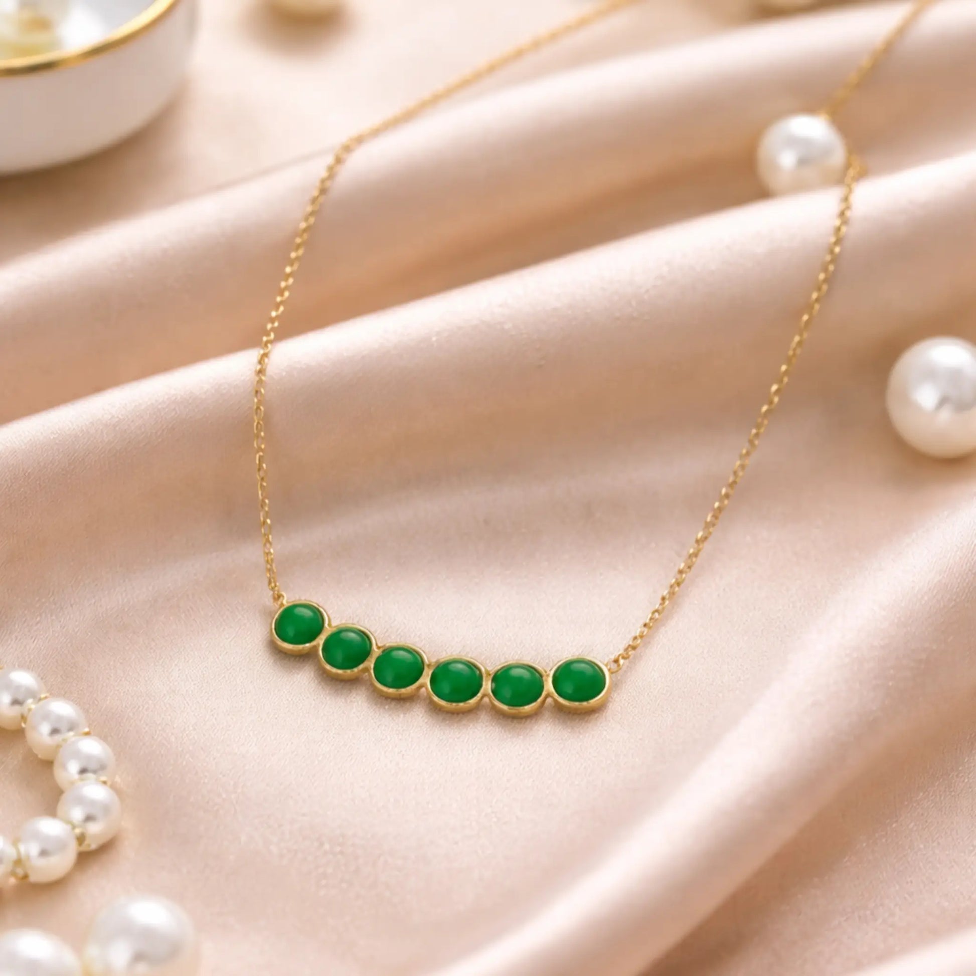 Gold necklace with green stones on a beige surface