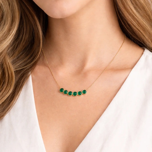 Gold necklace with green gemstones worn by a person against a neutral background