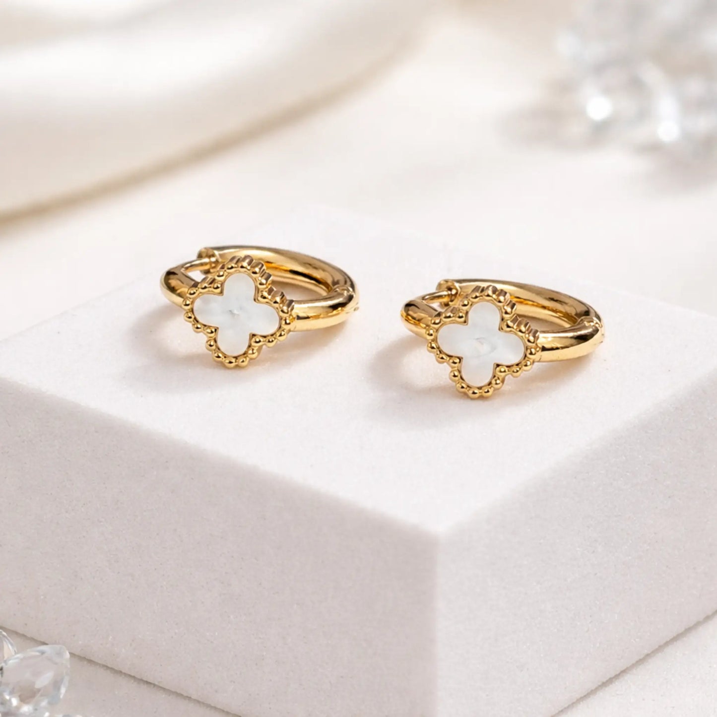 Close-up of YUBIRAA Eterna Bloom hoop earrings highlighting white clover detailing and premium gold polish finish