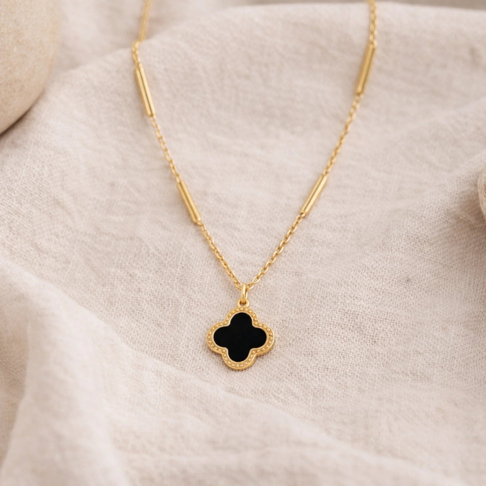 Yubiraa Final Ivory Glow Clover Necklace with black clover pendant styled on soft fabric for lifestyle aesthetic