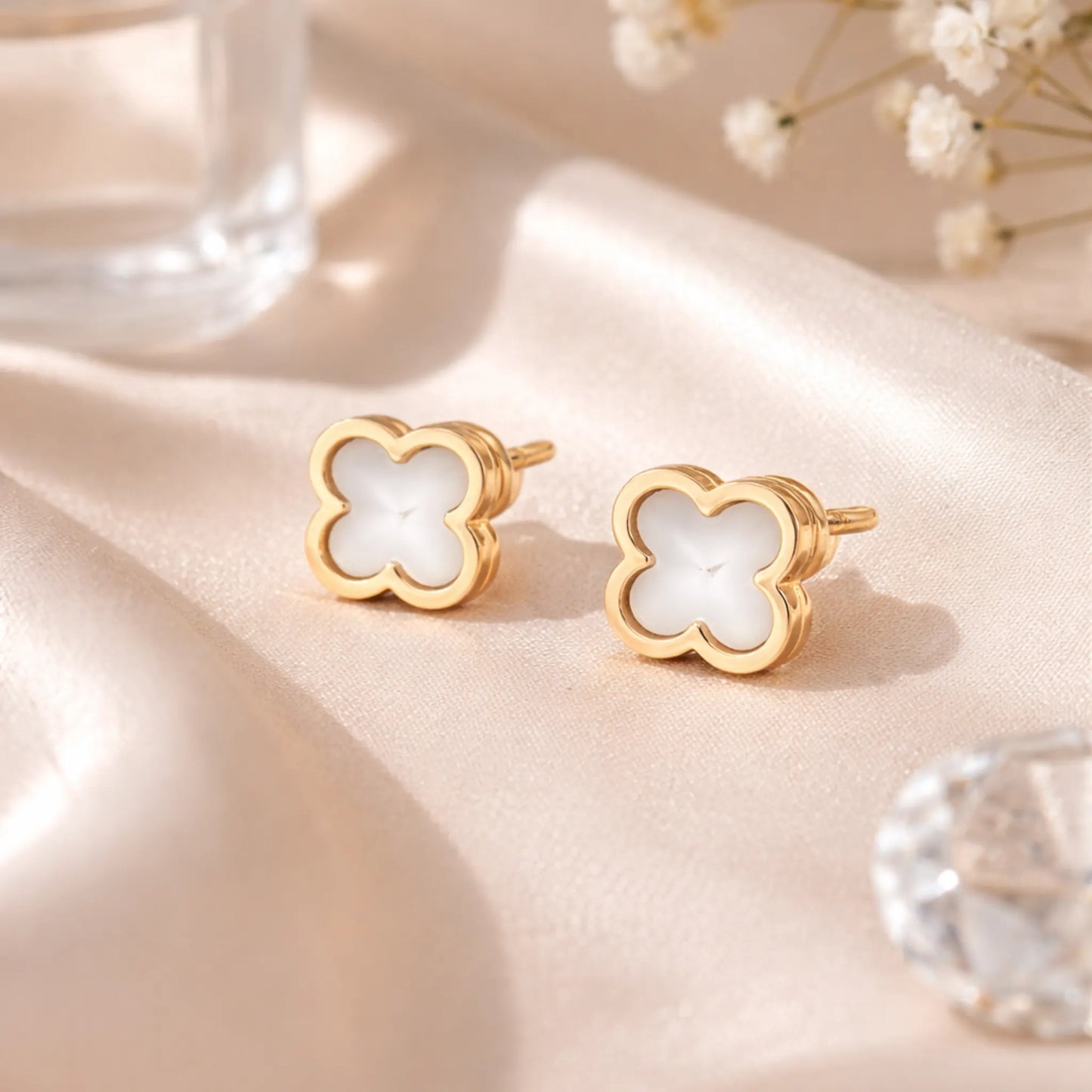 Yubiraa white clover stud earrings styled on satin fabric, gold plated anti tarnish floral earrings luxury aesthetic